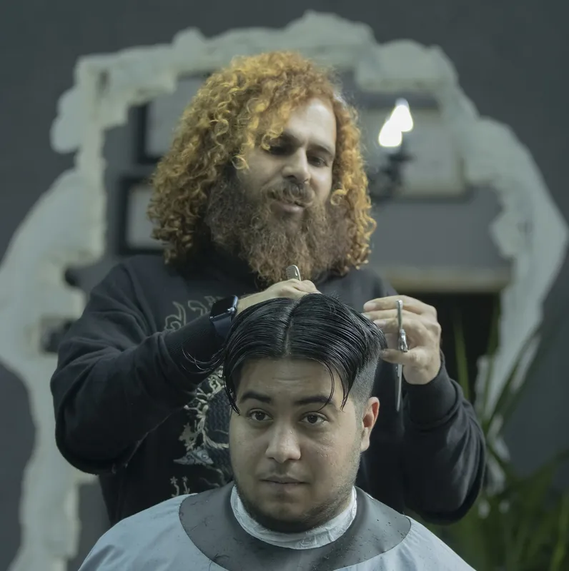 Barbier knipt een klant met donker, achterover gekamd haar
