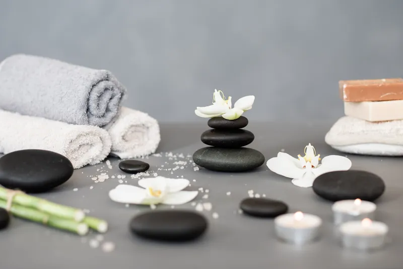 Massagestenen, opgerolde handdoeken en orchideeën op een behandeltafel